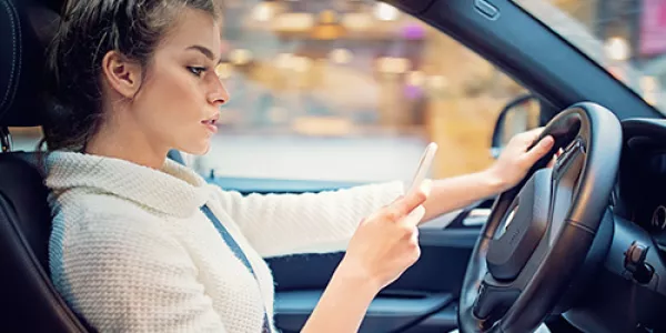 Woman driving and texting on mobile phone with one hand on steering wheel