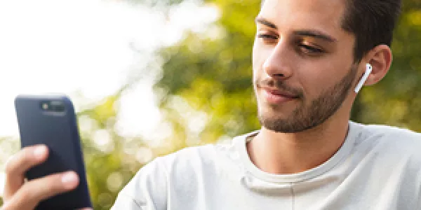 Person sitting in park using mobile phone and wireless earbuds