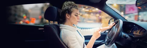 Woman driving and texting on mobile phone with one hand on steering wheel