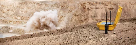 Foreground: Detonator box of yellow color intended for detonating explosives; Background: Mining blast at an open pit copper mine