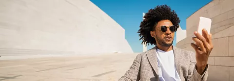 Man holding mobile phone, video calling in open air in a desert-like environment